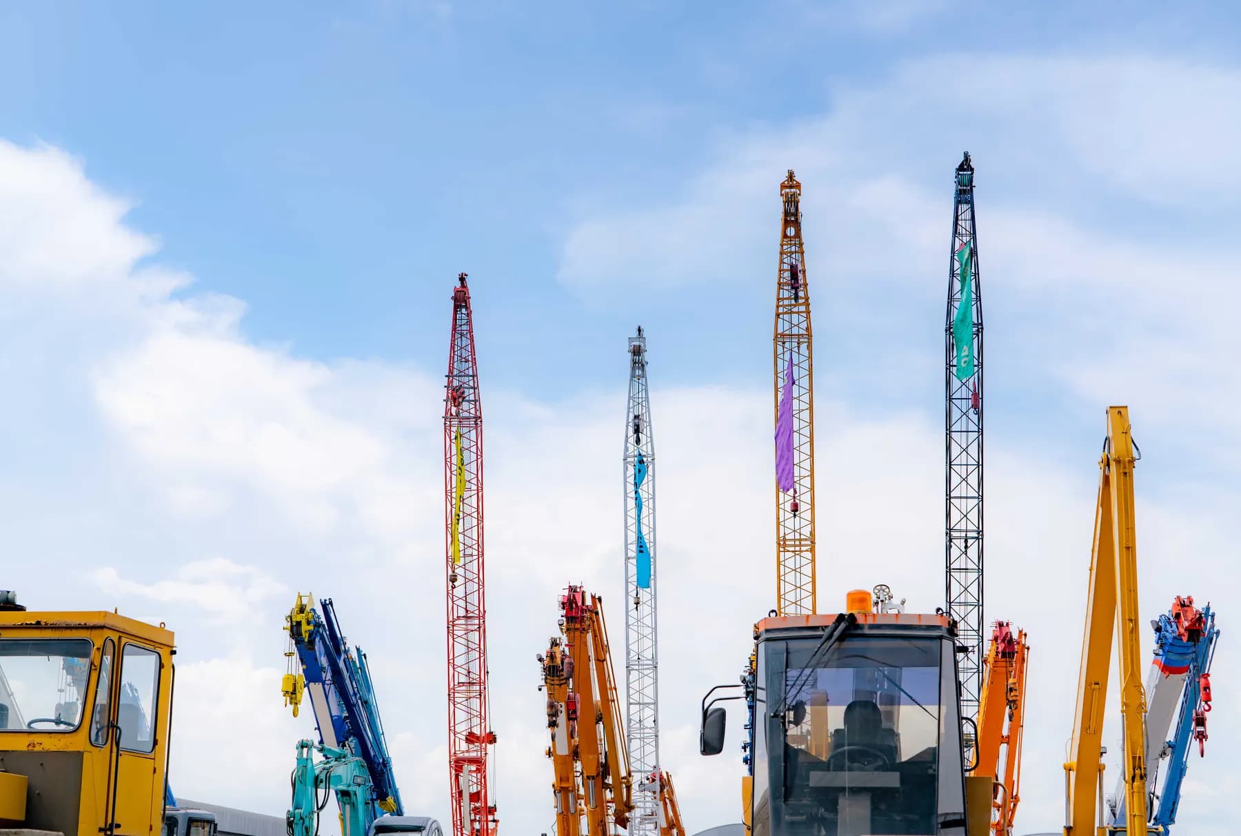 A fleet of cranes and heavy equipment lined up against a bright sky