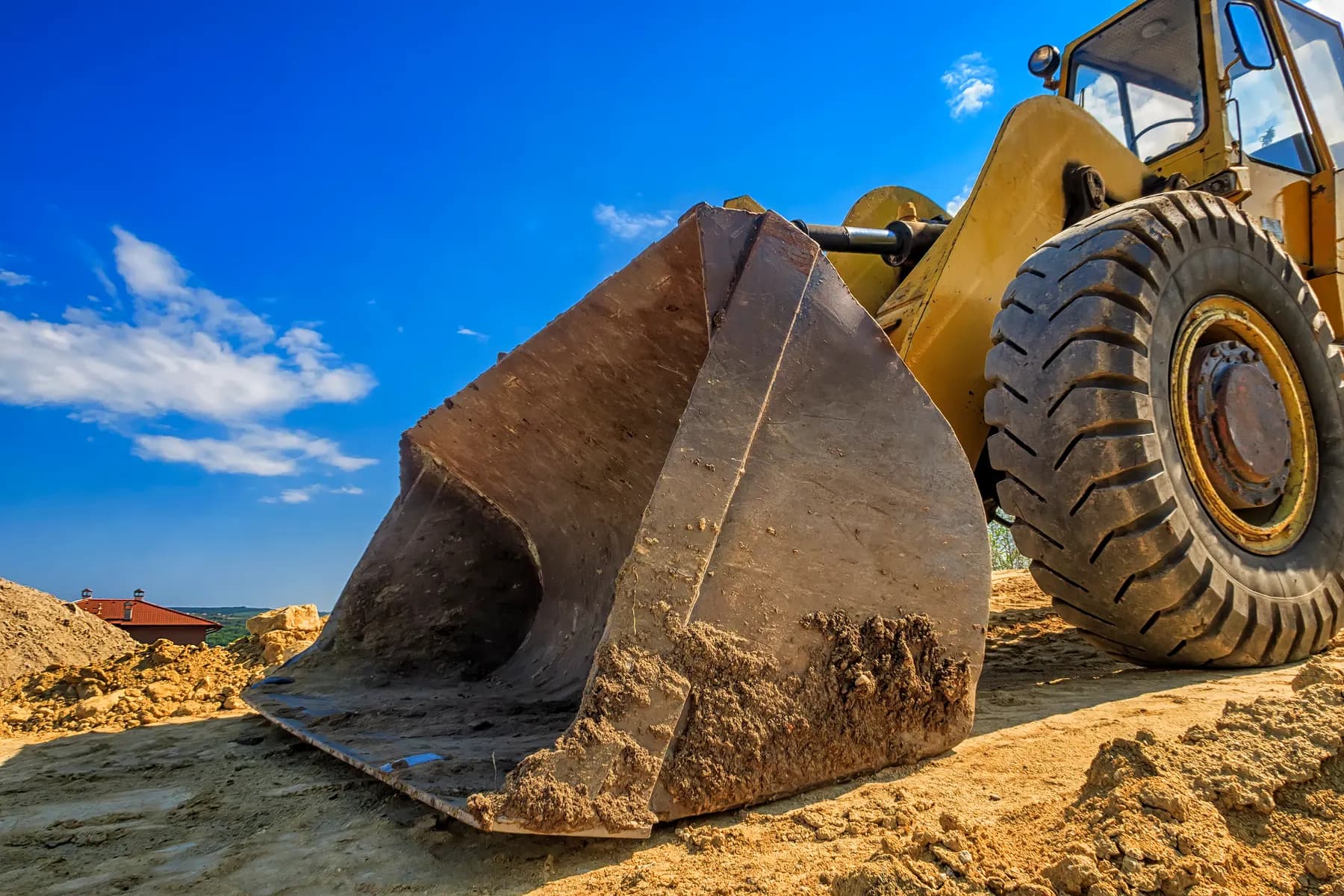 The bucket of a large yellow wheel loader resting in dirt